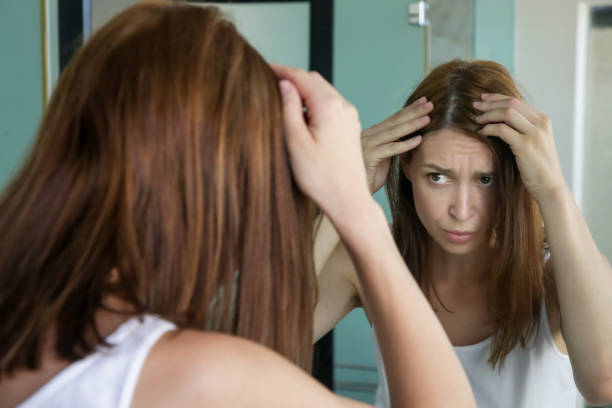 verticale d'une belle jeune femme examinant son cuir chevelu et cheveux devant le miroir, les racines de cheveux, la couleur, le cheveu gris, la perte de cheveux ou le problème sec de cuir chevelu - cheveux blancs photos et images de collection