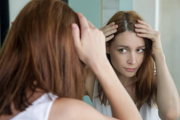 retrato de uma mulher nova bonita que examina seu escalpe e cabelo na frente do espelho, raizes do cabelo, cor, cabelo cinzento, perda de cabelo ou problema seco do escalpe - cabelo humano - fotografias e filmes do acervo