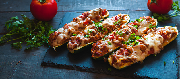 Homemade stuffed zucchini boats with ground beef, spicy tomato sauce, cheese and fresh parsley, on dark background