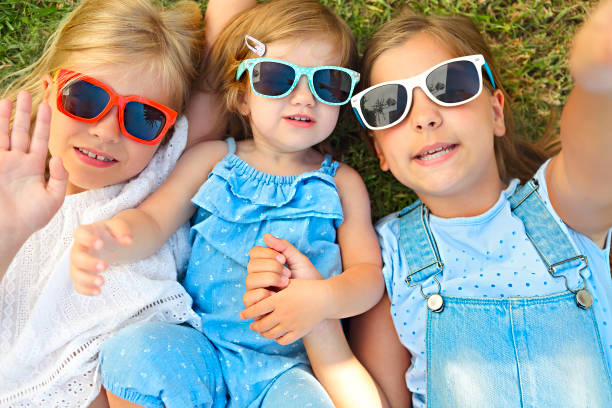 Laughing children wearing sunglasses relaxing during summer day on the green grass