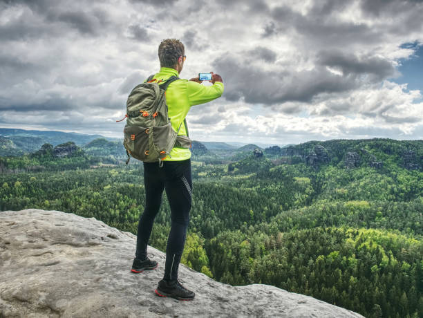 Trail runner takes rest, makes photos by his smart phone. Trail runner takes rest, makes photos by his smart phone. View into spring forest valley below low mountains. Spring trek. ultralight photos stock pictures, royalty-free photos & images