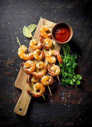 Shrimps with parsley, lime slices and tomato sauce. On dark rustic background