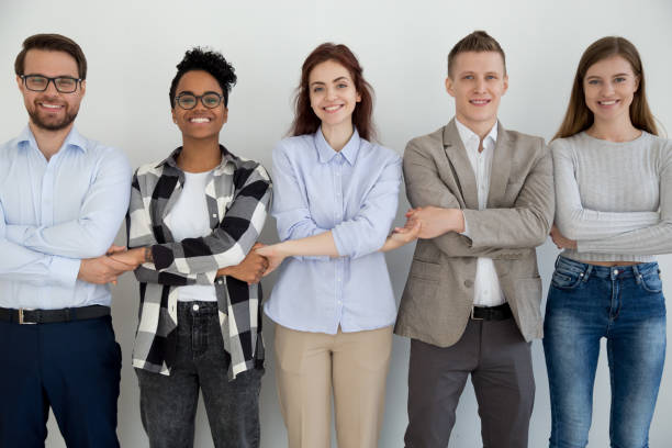 Happy diverse people standing holding hands together Five cheerful diverse multiracial millennial businesspeople students holding hands standing opposite wall smiling and looking at camera. Team building unity support teamwork or common goal concept five people photos stock pictures, royalty-free photos & images