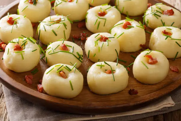 Photo of Polish authentic kluski potato dumplings with bacon and green onions close-up on a plate. horizontal