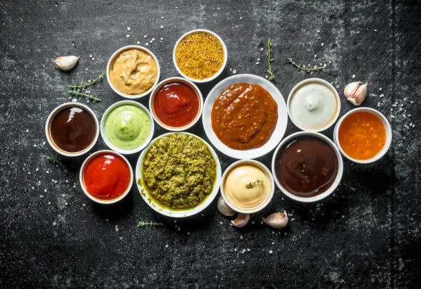 Photo of Pesto sauce, guacomole, ketchup, mustard, barbecue sauce in bowls.