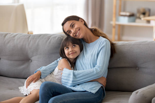 istock Cute happy daughter hug young mommy sitting on couch 1156092017