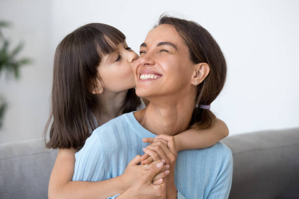 Cute little daughter kiss happy mom on cheek Cute small daughter kiss happy mom on cheek hugging her from behind, funny little caring preschooler kid piggyback embrace smiling mother showing love, child girl and mommy have sweet moment together cheek stock pictures, royalty-free photos & images