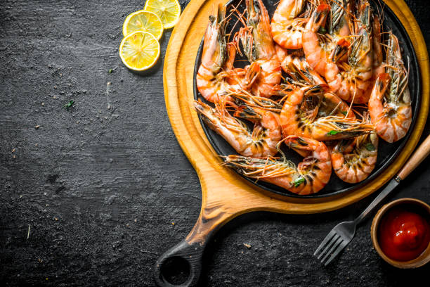 istock Grilled shrimps on a cutting Board with tomato sauce and sliced lemon. 1156092373