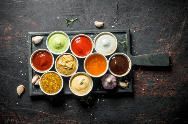 Different types of sauces in bowls on a cutting Board with garlic. On dark rustic background