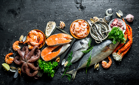 Fresh salmon steak with a variety of seafood and herbs. On black rustic background