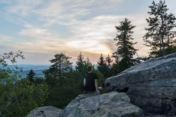 istock Young man sitting on stone rock in czech landscape with trees at sunset 1156096509