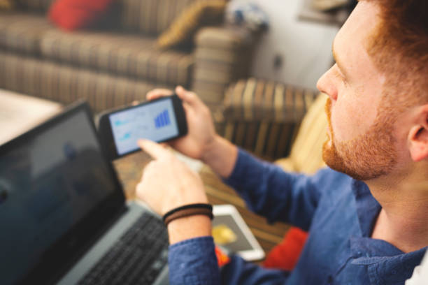 istock Man using laptop and looking at cell phone and seeing graphs 1156099859
