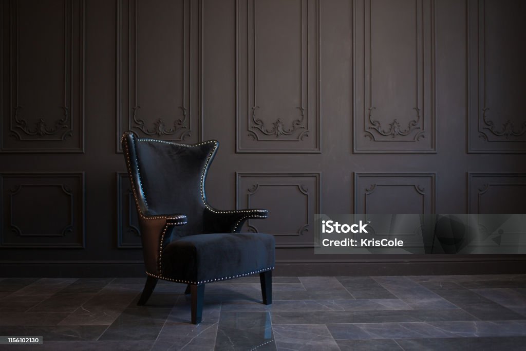 Stylish black chair against a dark gray wall Stylish black chair against a dark gray wall. Stylish chair on wall background, copy space, fashionable interior Chair Stock Photo