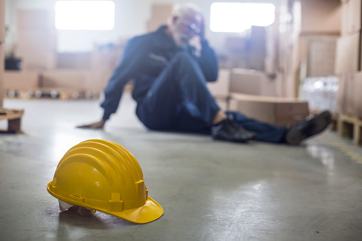 Warehouse worker sitting on a warehouse floor fallen from injury. About 60 years old, Caucasian senior male.