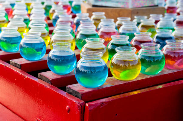 Jars Filled with Colorful Liquids as Part of a Midway Carnival Booth These colorful glass jars are filled with different colored liquids.  They were part of a carnival booth in which a contestant tried to get a pingpong ball to land inside one of the jars.  Winners got to take home a goldfish in a plastic bag. midway fair stock pictures, royalty-free photos & images