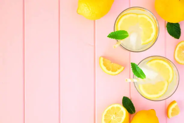 Photo of Summer lemonade, top view side border on a pastel pink wood background