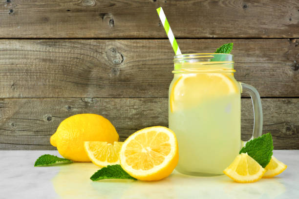 Lemonade in a mason jar glass with lemons, side view against rustic wood Homemade lemonade in a mason jar glass with lemons. Side view on a rustic wood background. mason jar lemonade stock pictures, royalty-free photos & images