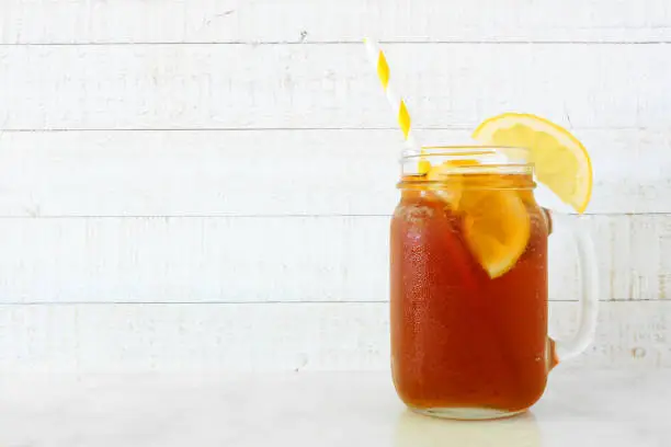 Summer iced tea in a mason jar glass. Side view on a white wood background.