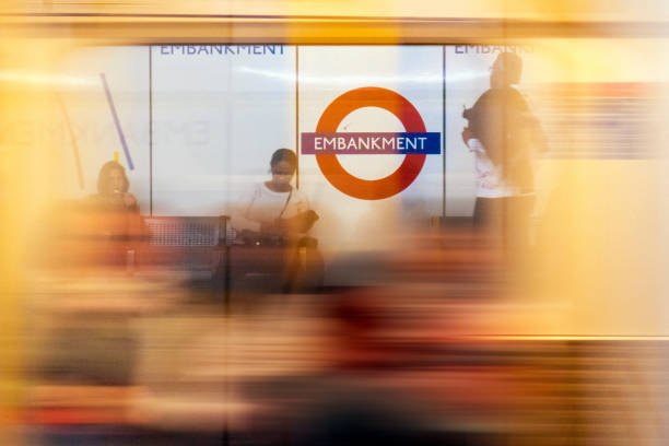 People waiting in the London subway while a train is passing by (high speed). The subway sign shows the name of the station: Embankment
