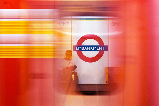 People waiting in the London subway while a train is passing by (high speed). The subway sign shows the name of the station: Embankment