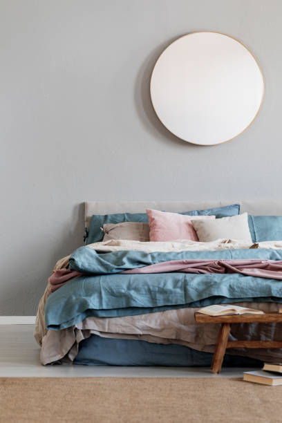 istock Classy round mirror on grey wall in stylish bedroom interior with warm bed with blue, pastel pink and beige bedding 1156141225