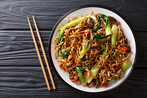 Asian vegetarian food udon noodles with baby bok choy, shiitake mushrooms, sesame and pepper close-up on a plate on the table. horizontal top view from above