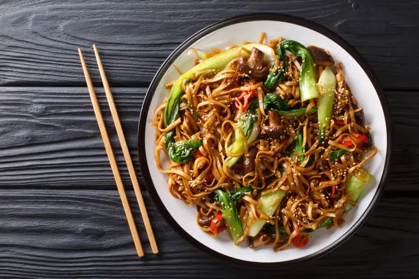 Asian vegetarian food udon noodles with baby bok choy, shiitake mushrooms, sesame and pepper close-up on a plate on the table. horizontal top view from above