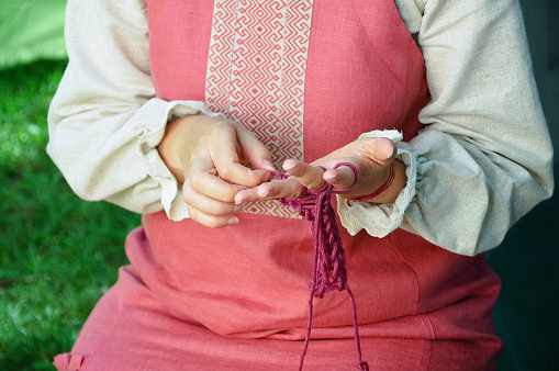 A girl in a national Russian costume knits out of wool on her fingers.