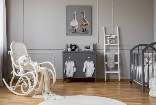 istock Baby clothes hanging on knobs on grey wooden commode in lovely nursery, copy space and poster on empty wall 1156143582
