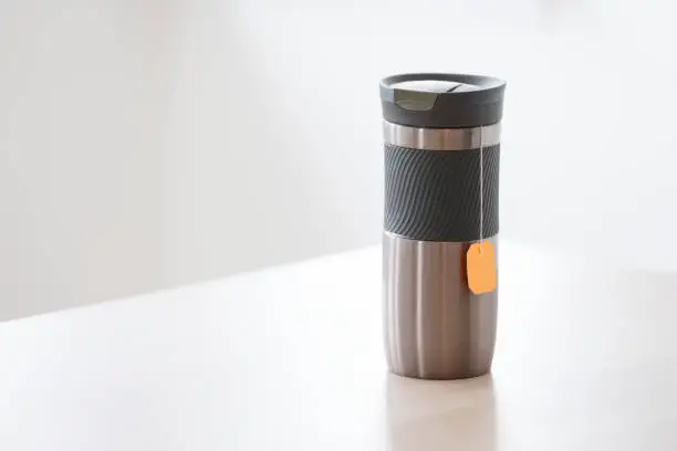 Travel thermal flask and hot tea drink with orange bag string hanging for travellers in outdoors with rubber grip uk