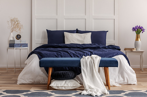 White blanket on velvet bench in the food of double bed