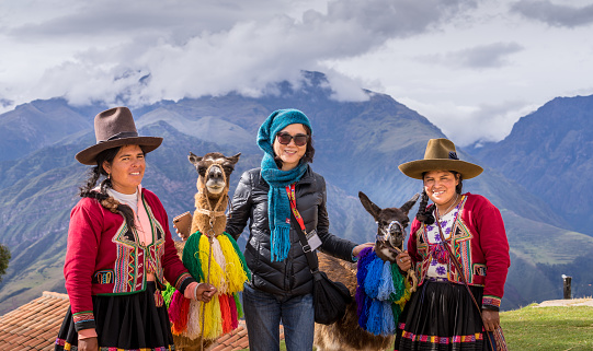 Cuzco, Peru - April 30, 2019. Peruvian women in traditional clothing with llama picturing with tourist