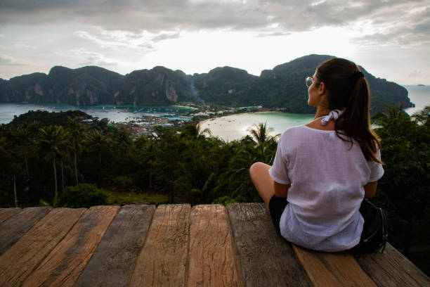 istock Beautiful woman sitting on wooden platform with Phi Phi island views and cloudy sky and copy space 1156145643