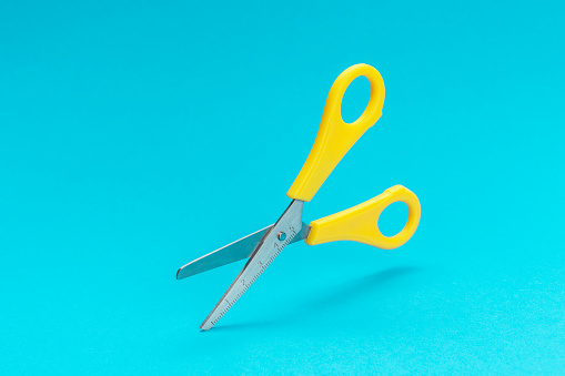 opened yellow scissors over turquoise blue background. conceptual photo of levitating scissors with central composition