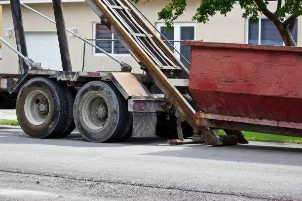 Empty construction dumpster being unloaded from truck at residential construction site