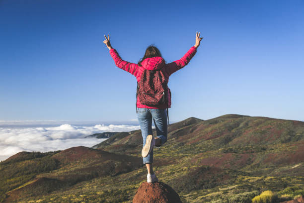istock Teenager with backpack and raised hands standing on a mountain cliffs edge with gorgeous view to forest sea and clouds Volcano Teide Tenerife Spain Adventure freedom tourism carefree and youth concept 1156163485