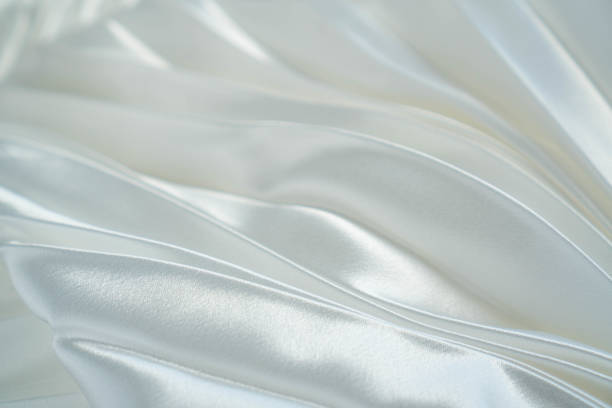 istock White luxury satin fabric waves background. Rippled white silk fabric satin cloth waves glamour background. Use for cosmetic store or spa salon. Wedding or Christmas background or New Year background design 1156169221