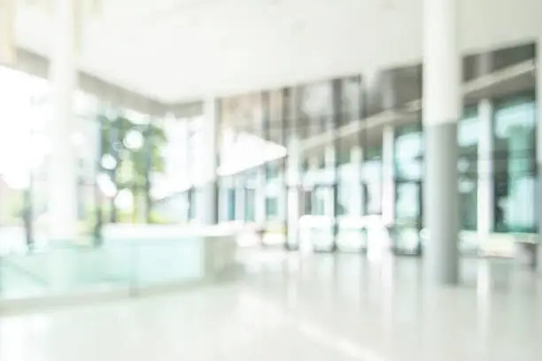 Hotel or office lobby blur background interior view toward reception hall, modern luxury white room space with blurry corridor and building glass wall window