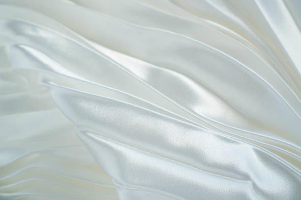istock White luxury satin fabric waves background. Rippled white silk fabric satin cloth waves glamour background. Use for cosmetic store or spa salon. Wedding or Christmas background or New Year background design 1156172158