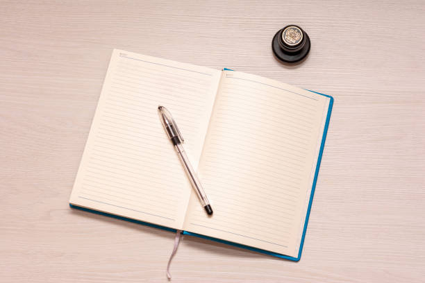 istock Opened notebook with black pen and official stamp on a white wooden table, top view 1156184386