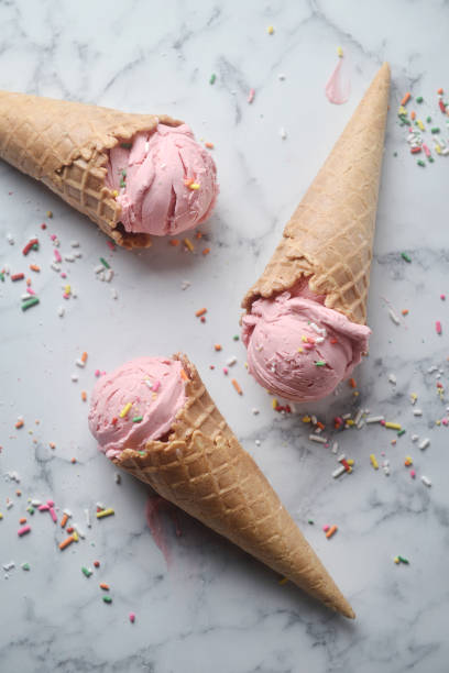 istock Delicious strawberry ice cream cone decorated with sugar rainbow sprinkles on marble background. top view 1156206485