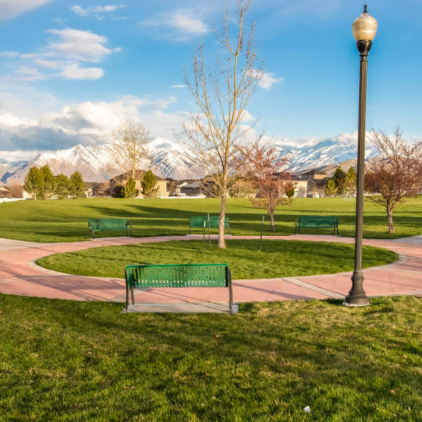 istock Square Green benches around a circular pathway on a park with trees and lamp posts 1156207272