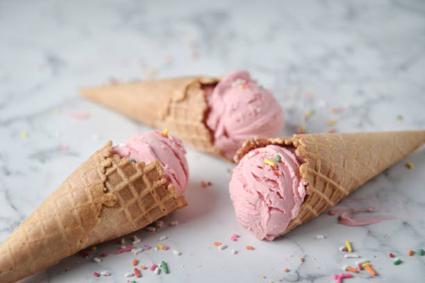 istock Delicious strawberry ice cream cone decorated with sugar rainbow sprinkles on marble background. 1156207375