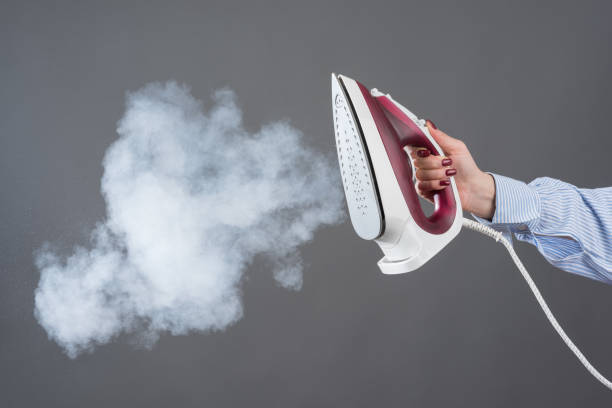istock Woman holds an iron with steam on gray background 1156210534