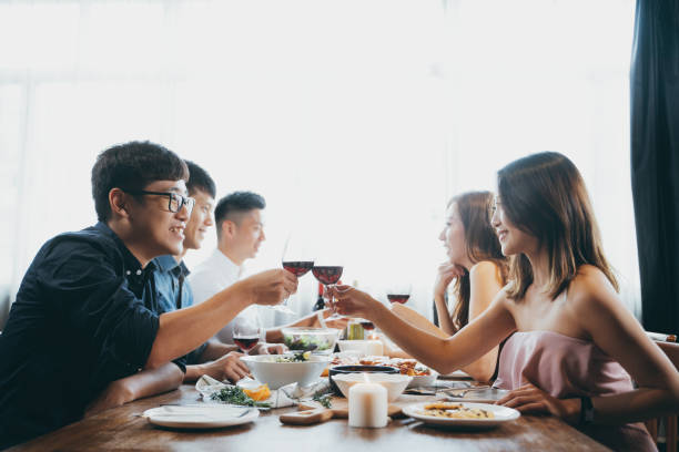 Group of joyful young Asian man and woman chatting, having fun and toasting with red wine during party Group of joyful young Asian man and woman chatting, having fun and toasting with red wine during party blind date stock pictures, royalty-free photos & images