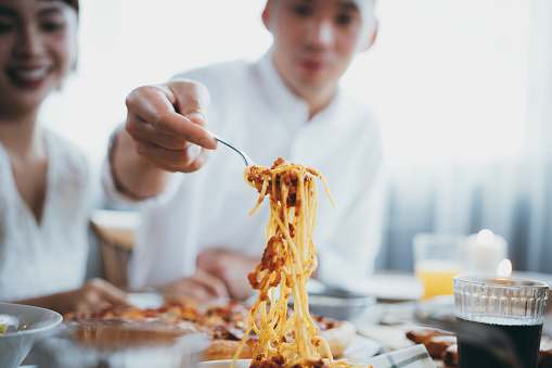Young Asian man serving pasta to friends during party, they are having fun, chatting and enjoying food and drinks