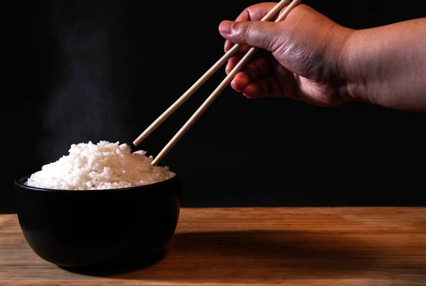istock Rice in a black bowl and smoke on a black background. 1156223872