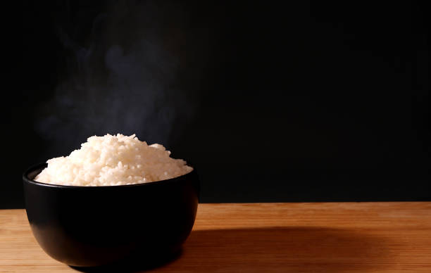 istock Rice in a black bowl and smoke on a black background. 1156223873