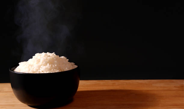 istock Rice in a black bowl and smoke on a black background. 1156223875