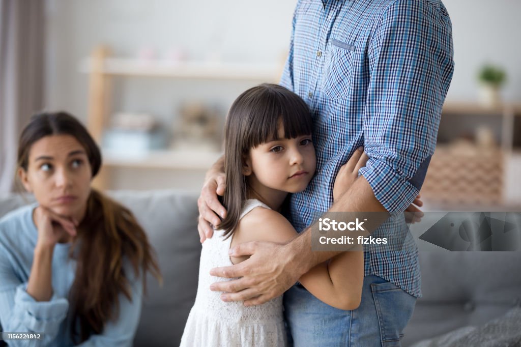Unhappy little child hug leaving parent say goodbye Sad little girl hug father upset by father leaving on business trip, unhappy young family in living room with preschooler daughter embrace say goodbye to father, parents divorce hurt small child Child Stock Photo